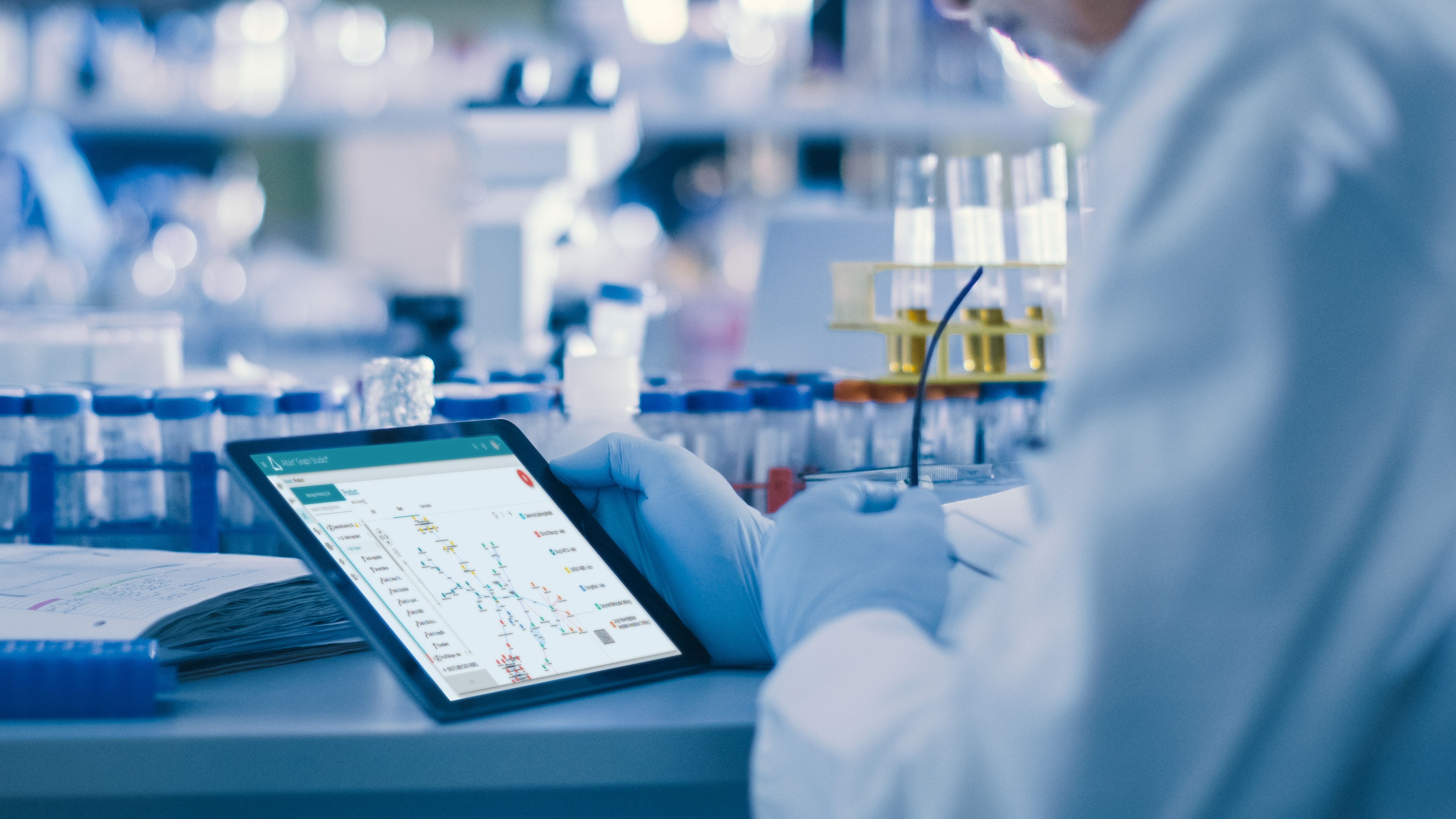 : A technician wearing a lab coat and gloves holds a tablet reviewing a Altair® Graph Studio™ knowledge graph in a lab environment.