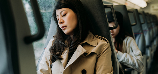 Traveler sleeping on a passenger train beside the window.