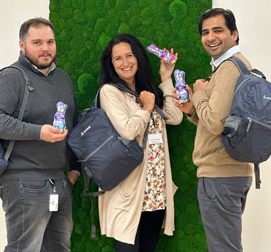 A small group of Altair employees holding chocolate bunny candy in front of a green moss wall.