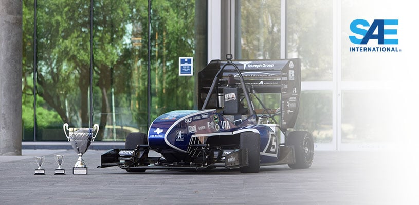 A photograph of an SAE Formula racing car on display in a showroom next to three trophies.
