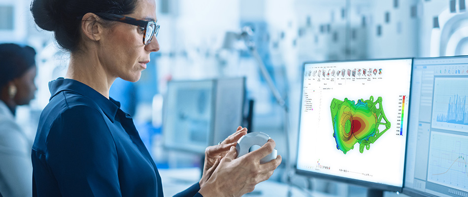 Professional woman with eyeglasses examining a physical object and a colorful simulation on a computer screen.