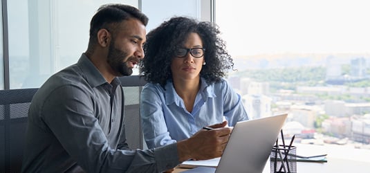 Two people using AI agents on laptop screen in office.