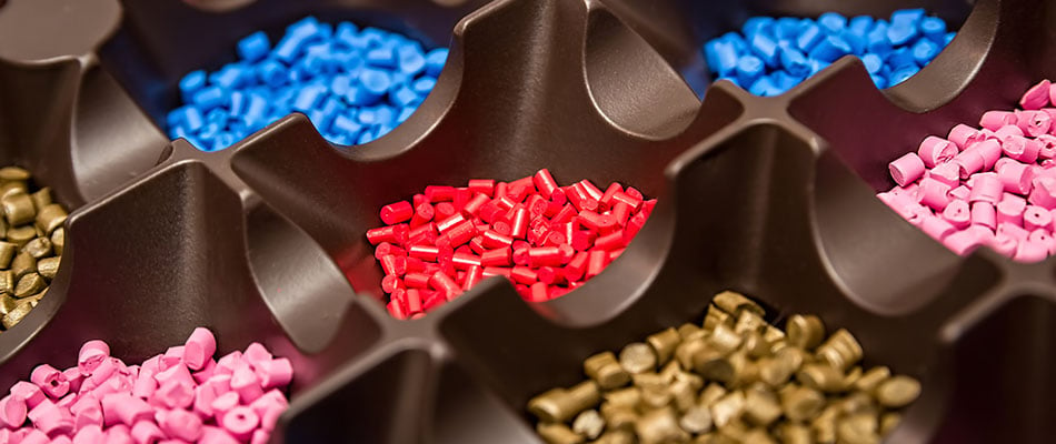 A photograph of a segmented tray containing hundreds of small, brightly colored polymeric dye plastic pellets.