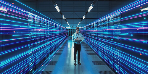 High-tech computing data center with an IT administrator using a laptop for HPC and cloud reporting.