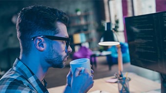 Man sitting at computer drinking from a cup.